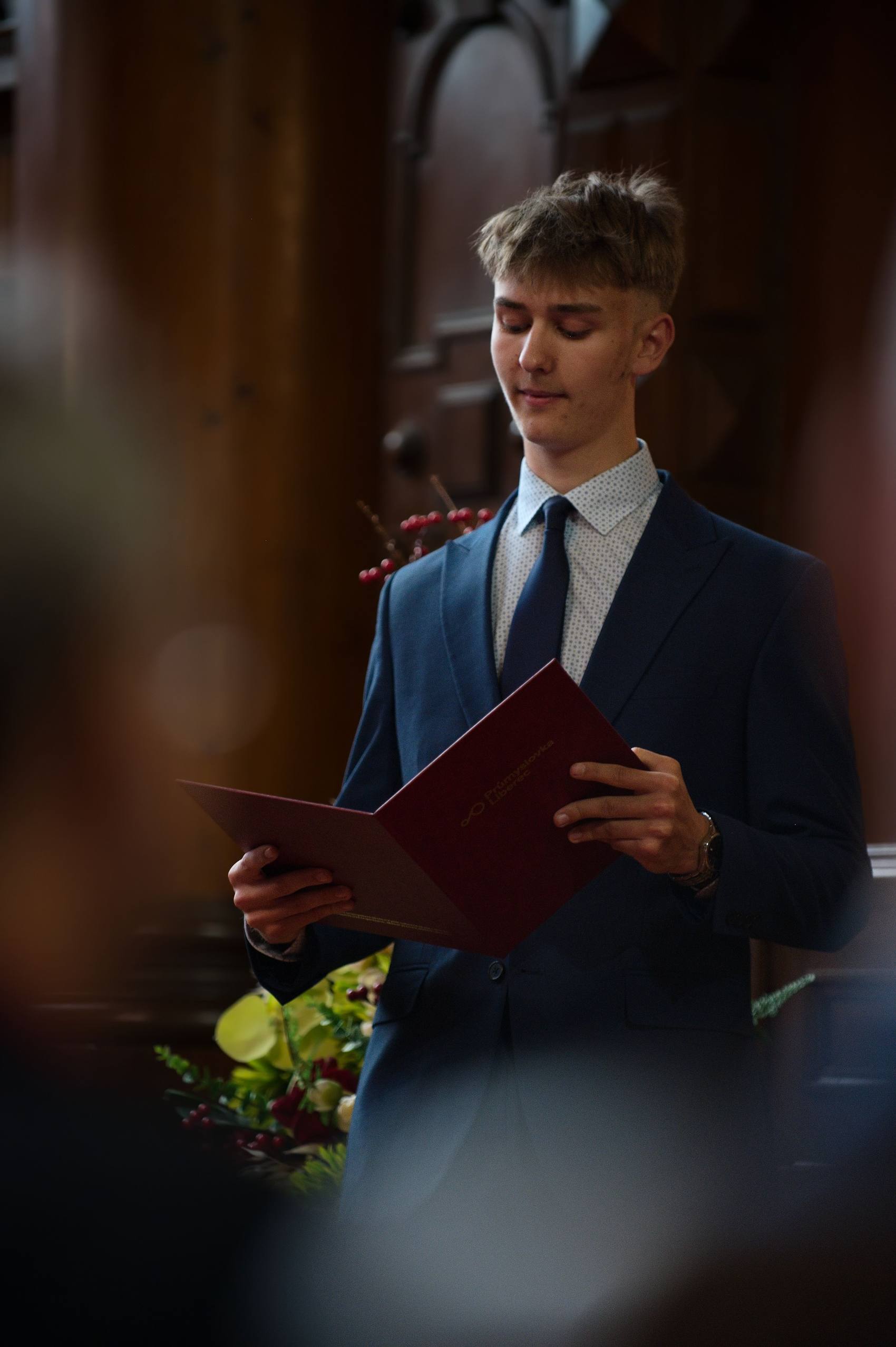 Maturant v obleku čte slavnostní projev z desek